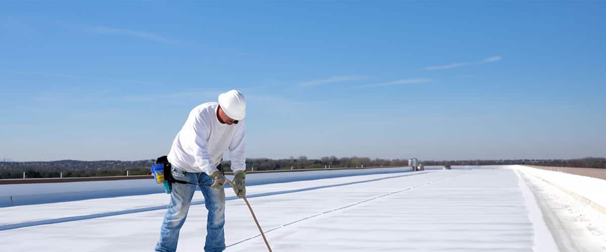 Worker applies an insulation coating on the concrete surface of a rooftop. Repairman fixing a leaking roof or deck by applying waterproofing solution